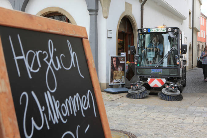 Tafel "Herzlich Willkommen" und Kehrmaschine im Hintergrund